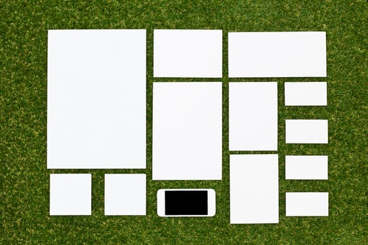 White paper sheets arranged neatly on a green grass surface with a smartphone placed among them for creative design purposes photo