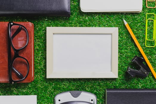 Collection of stationary items arranged on green grass with empty frame and office tools at midday photo