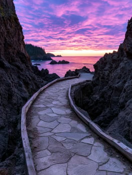A scenic stone path leads to the ocean under a vibrant sunset sky photo