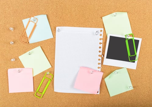 Creative workspace setup with colorful sticky notes, paper clips, and a blank notepad on a corkboard photo