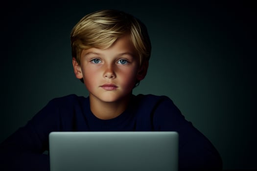 Young child focused on laptop screen in a dimly lit room, illustrating concentration and curiosity photo
