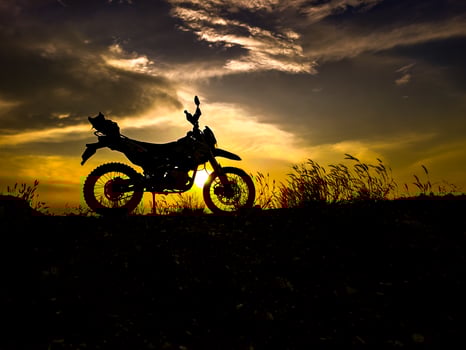 Silhouette of a Motorcycle Against a Dramatic Sunset Sky with Grassy Hill in the Foreground photo