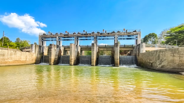 Scenic View of a Modern Dam with Flowing Water Under a Clear Blue Sky Surrounded by Lush Greenery and Concrete Structures photo