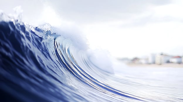 Majestic ocean wave crashing against the shore, with a serene beach and distant buildings visible photo