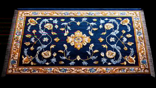 Ornate blue and gold floral rug displayed on a dark background, showcasing intricate embroidery photo