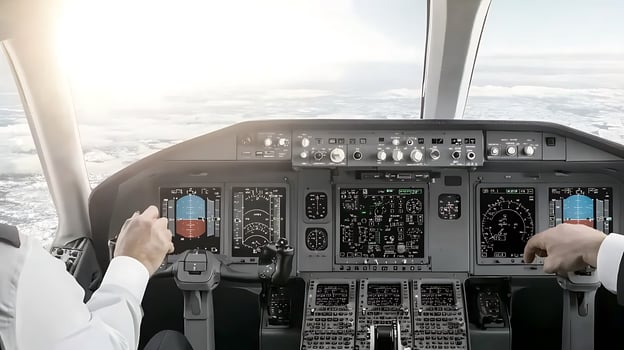 Pilot operating aircraft controls in cockpit with instruments and clouds visible outside photo