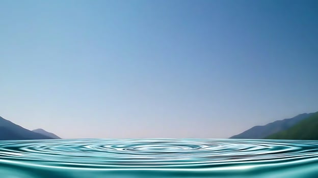 Serene landscape featuring calm water ripples under a clear blue sky with distant mountains photo
