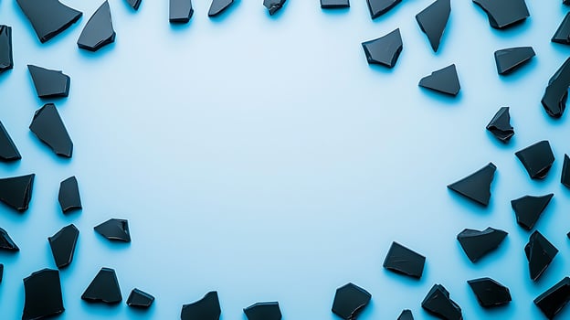 Shattered black glass pieces scattered on a light blue background, creating a modern abstract frame photo