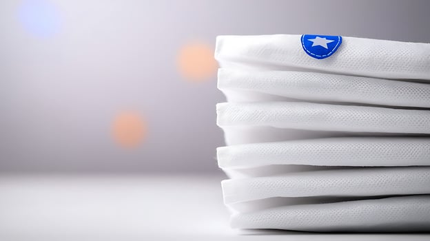 Stacked white towels with a blue emblem against a softly blurred background of warm lights photo