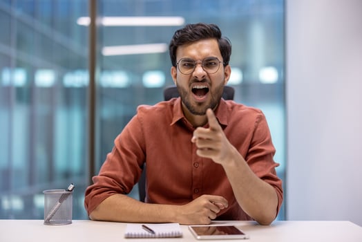 Hispanic businessman expressing frustration at desk, pointing assertively. Modern office setting with open background. Emotion conveyed through gestures, creating dynamic and intense atmosphere. photo