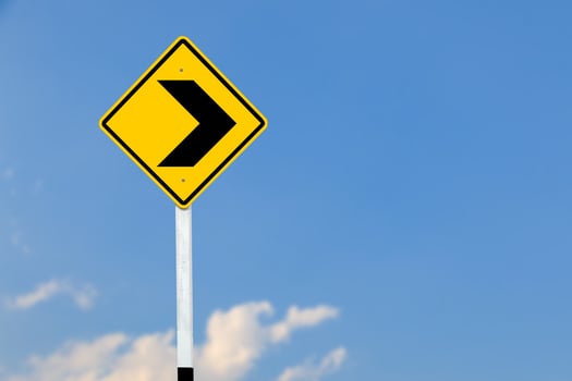 Black right direction symbol is displayed on a bright yellow traffic sign on blurred sky background. photo