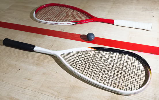 Two rackets and two squash balls lie on the parquet floor. Horizontal photo