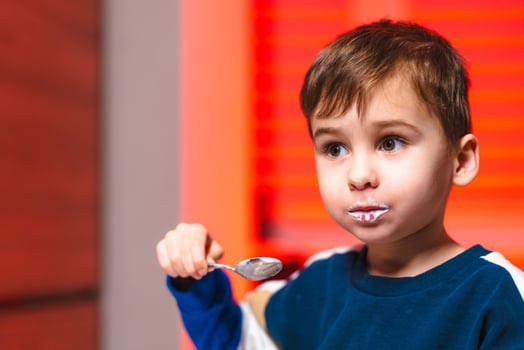 Young boy enjoying ice cream at home. A child with a messy face happily savors a spoonful of ice cream while seated indoors with warm lighting. photo