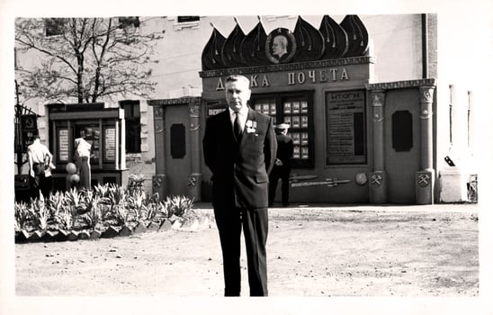Vintage portrait of an elderly man in the uniform of a USSR railway worker near the honor board. The inscription on the Russian Honor Board. photo