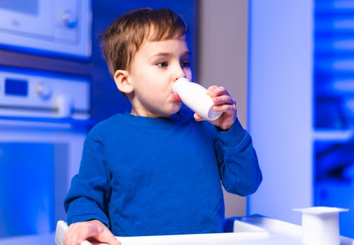 Child drinks in cozy kitchen. A young child wearing a blue shirt sips from a small cup in a modern kitchen with blue lighting. photo