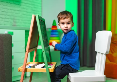 Child painting in bright room. A young child focused on drawing at a small easel in a bright, playful room filled with colorful decor. photo