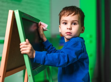 Boy erasing chalkboard in class. A young boy wears a blue shirt as he wipes a chalkboard in a bright, colorful classroom setting. photo