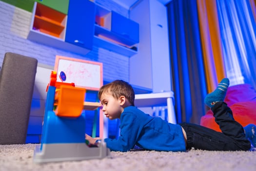 Boy playing with toy in living room. A young boy lies on the carpet, focused on a colorful toy in a bright living room with playful decor. photo