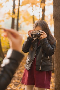 Child taking picture her mother on retro camera in autumn park. Hobbies and leisure concept. photo
