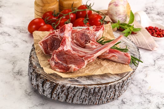 Raw lamb chops on a wooden board with tomatoes and herbs photo