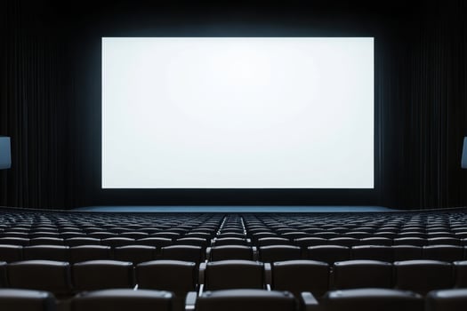 Rows of empty theater seats face a large, bright white screen in anticipation of a film photo