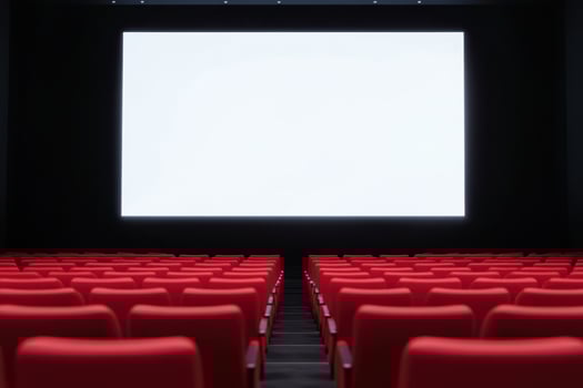 Rows of unoccupied red seats face a bright, blank screen in a dark movie theater setting photo