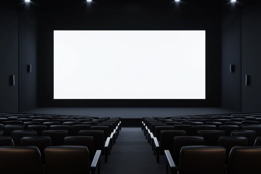 An empty, dark movie theater with rows of seats facing a bright white screen, awaiting viewers photo