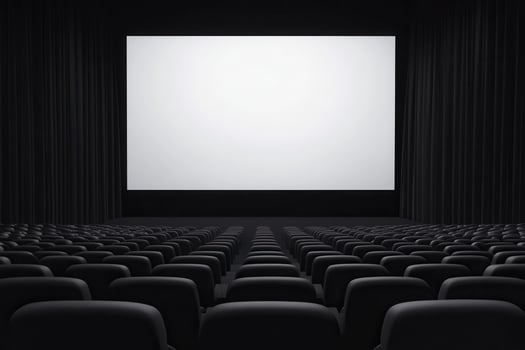 Rows of empty dark seats face a large bright white screen in a spacious viewing theater photo