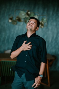 Man in dark shirt feeling grateful with hand on chest and eyes closed photo