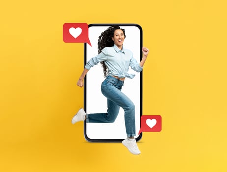 A lively woman is joyfully leaping out of a smartphone, surrounded by red heart icons, symbolizing connection and affection. The bright yellow background enhances the cheerful vibe. photo