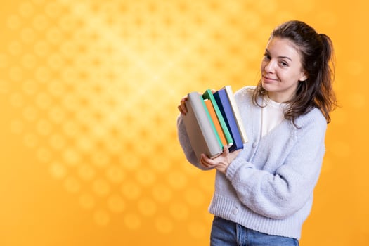 Portrait of cheerful woman carrying stack of textbooks, gathering information for school exam, isolated over studio background. Smiling pupil holding pile of books, preparing for university assessment photo