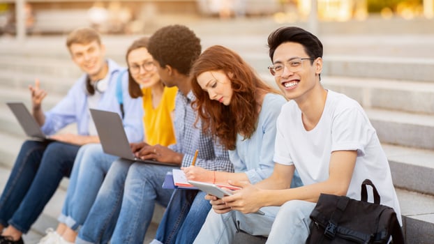 Teamwork Concept. Multiethnic students sitting on steps and learning, asian boy looking at camera photo