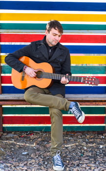 young man playing guitar and sitting against colorful wall photo