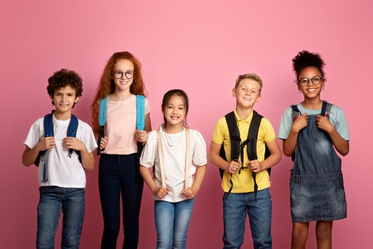 Back to school again. Joyful children with backpacks standing together on pink background photo