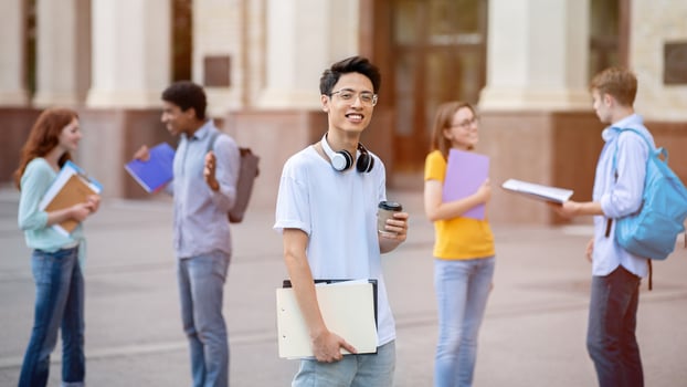 Asian Student Guy Standing Among Multiethnic Students Near University Building Outside, Smiling To Camera. Higher Education photo