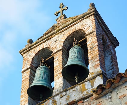 Two bells hanging in a brick bell tower under a cross photo