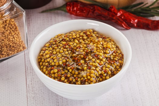 A bowl of mustard and a jar of chili peppers photo