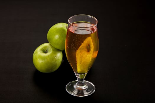 A glass of liquid next to a bunch of green apples photo