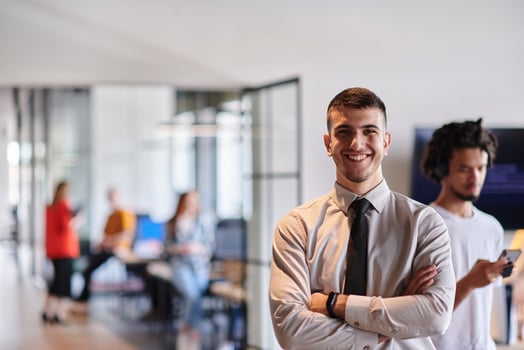 A young business leader stands with crossed arms in a modern office hallway, radiating confidence and a sense of purpose, embodying a dynamic and inspirational presence. photo
