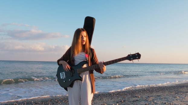 Girl Walks And Plays The Bass Instrument On The Beach Near The Ocean At Sunset photo