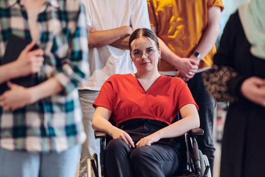 A diverse group of young business people congregates within a modern startup's glass-enclosed office, featuring inclusivity with a person in a wheelchair, an African American young man , and a hijab photo