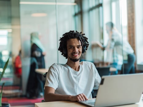 An African-American male, utilizing adaptive technology in his wheelchair, seamlessly integrates into a modern office space, embodying inclusivity and independence as he engages with a laptop photo