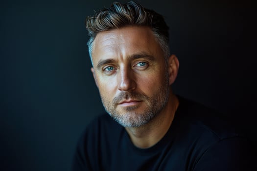 Man with blue eyes and short gray hair poses against a dark background in a simple black shirt photo