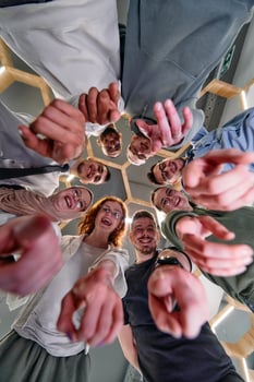 A group of cheerful young people gathered in a circle, pointing at the camera from a low-angle perspective. photo