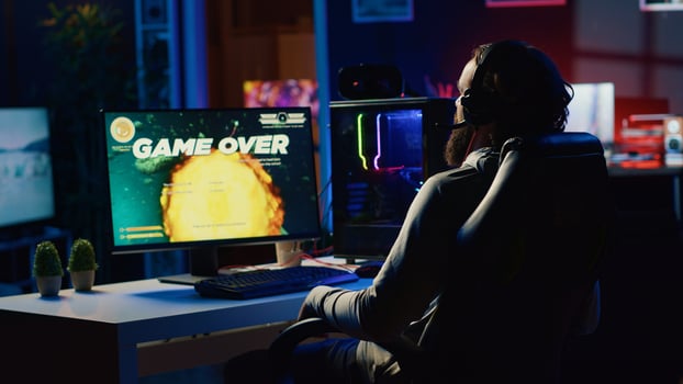 Upset gamer hitting desk in frustration after receiving game over screen, getting his spaceship destroyed in flying game. Sad player feeling disappointed after losing science fiction videogame photo
