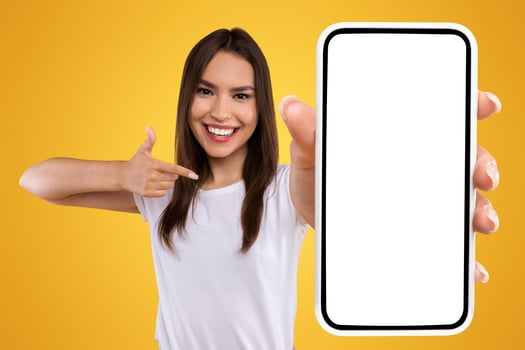 Check This Website. Portrait of smiling female holding smartphone with white blank screen in hand, showing device close up to camera and pointing finger at gadget with empty free space for mock up photo