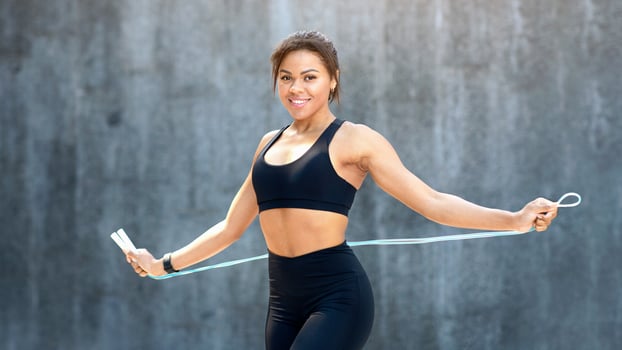 Smiling african fitness model holding skipping rope over grey wall at park, fitness concept, copy space photo