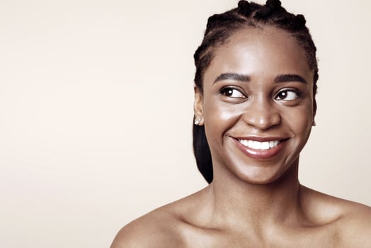 Closeup portrait of naked attractive young black lady smiling and looking at copy space for advertisement over beige studio background. Feminine beauty, beautiful body and face concept photo