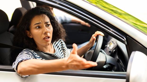 Indignant brunette lady driver fighting on the road, looking through car window, gesturing and yelling, woman got stuck in traffic or collided on the road, travelling with her boyfriend, side view photo