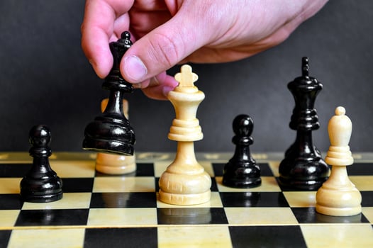 Male hand holding the black queen to defeat the white king on a chessboard on black background. Checkmate photo